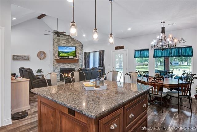 kitchen with decorative light fixtures, a stone fireplace, dark wood-type flooring, and lofted ceiling