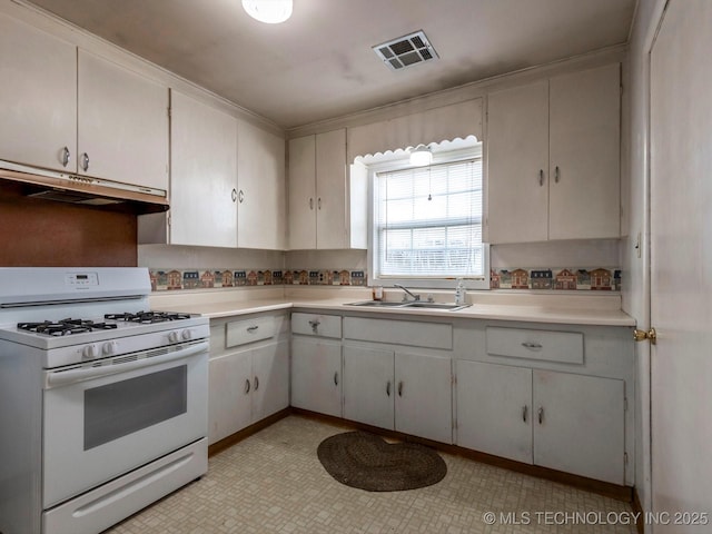 kitchen with white range with gas stovetop, backsplash, white cabinets, and sink