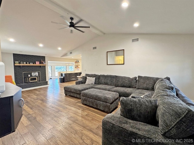 living room featuring ceiling fan, a brick fireplace, wood-type flooring, and lofted ceiling with beams