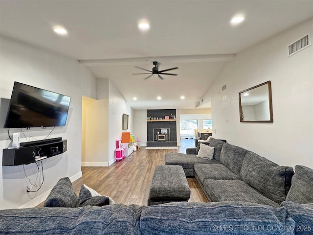 living room with ceiling fan, hardwood / wood-style flooring, lofted ceiling with beams, and a brick fireplace