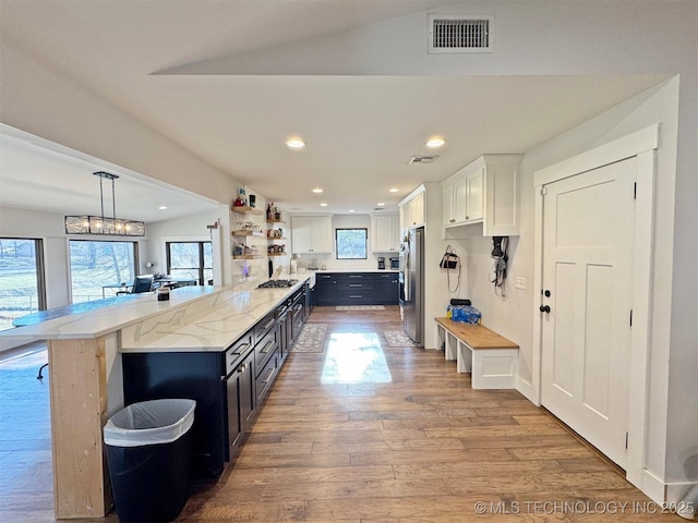 kitchen with pendant lighting, white cabinetry, stainless steel appliances, light hardwood / wood-style floors, and vaulted ceiling