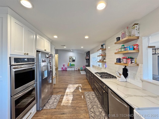 kitchen with white cabinets, dark wood-type flooring, light stone countertops, decorative backsplash, and stainless steel appliances