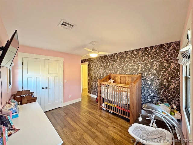 bedroom with hardwood / wood-style floors, a closet, ceiling fan, and a nursery area