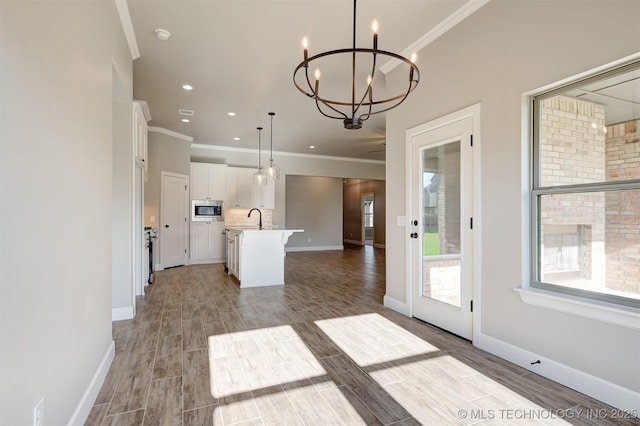 kitchen featuring white cabinets, decorative light fixtures, an inviting chandelier, an island with sink, and stainless steel microwave