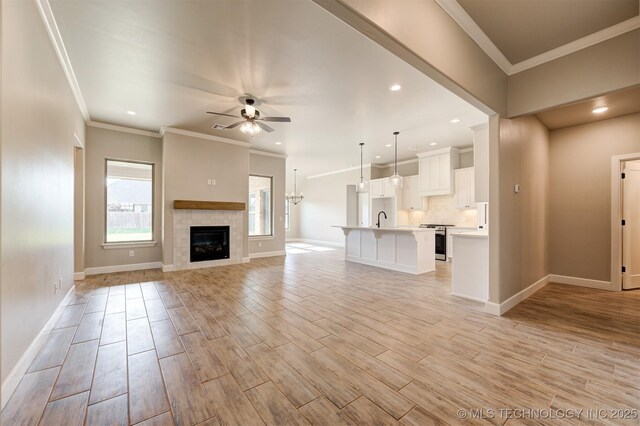 unfurnished living room with ceiling fan, sink, a tile fireplace, and ornamental molding