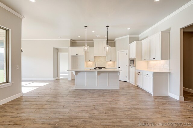 kitchen with decorative light fixtures, a center island with sink, white cabinetry, and stainless steel microwave