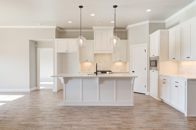 kitchen featuring white cabinets, a kitchen island with sink, stainless steel microwave, and hanging light fixtures