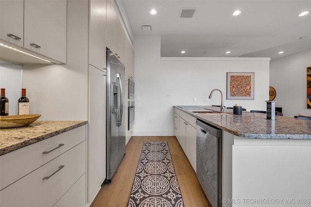 kitchen with stainless steel appliances, light stone countertops, sink, and light wood-type flooring