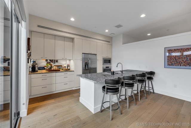 kitchen with stainless steel appliances, dark stone countertops, a kitchen breakfast bar, and light hardwood / wood-style floors