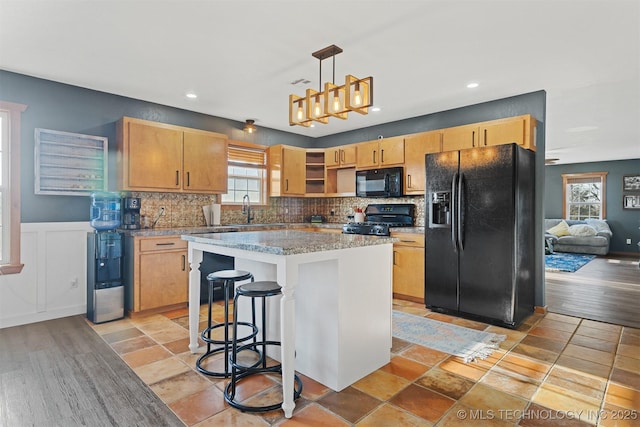 kitchen with pendant lighting, black appliances, a healthy amount of sunlight, and a kitchen island