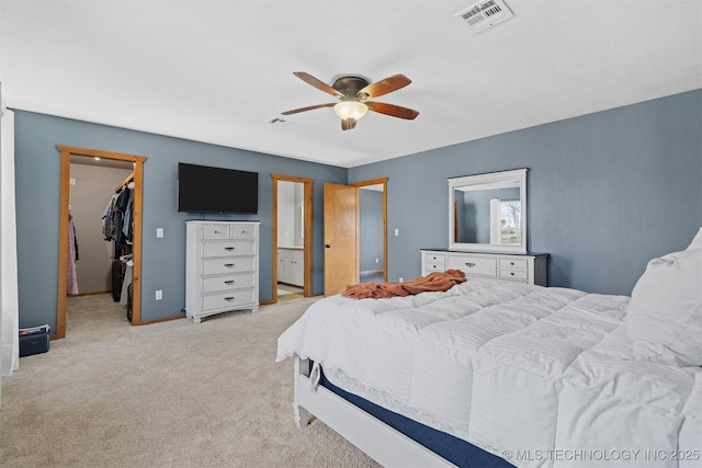 bedroom with connected bathroom, a spacious closet, light carpet, a closet, and ceiling fan