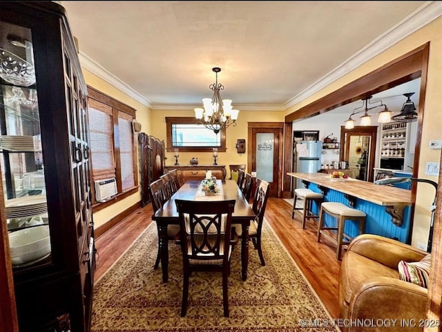 dining space with hardwood / wood-style flooring, crown molding, cooling unit, and a chandelier