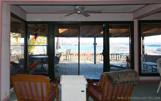 sunroom featuring a view of the beach, ceiling fan, and a water view