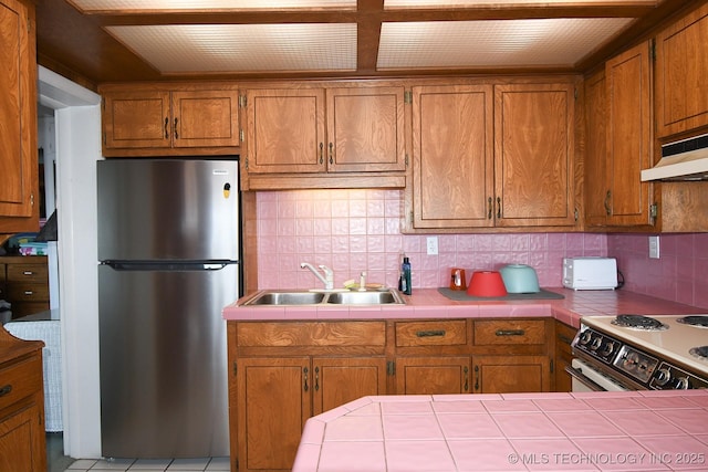 kitchen with sink, stainless steel fridge, electric range oven, tile counters, and decorative backsplash