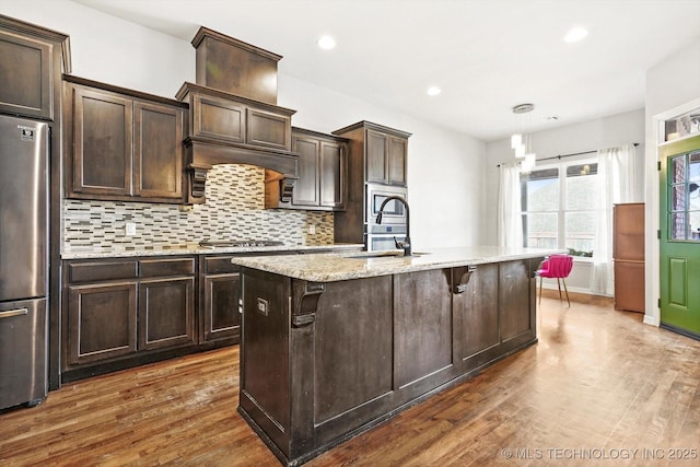 kitchen with a kitchen bar, stainless steel appliances, sink, hanging light fixtures, and a kitchen island with sink