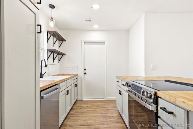 kitchen featuring wood counters, white cabinetry, stainless steel appliances, sink, and hanging light fixtures