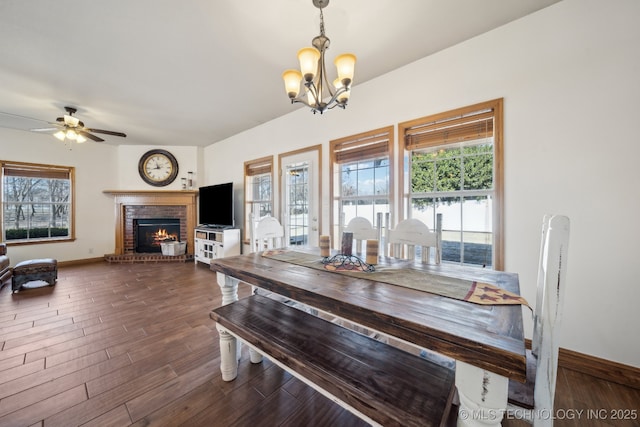 dining room featuring ceiling fan with notable chandelier, dark wood-type flooring, and a fireplace