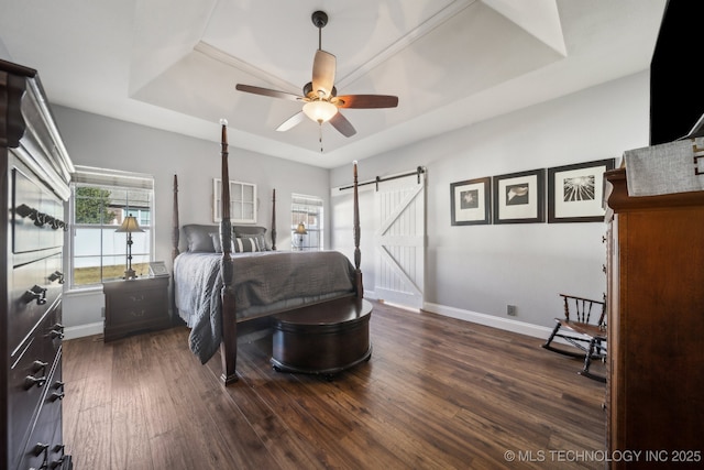 bedroom with a barn door, ceiling fan, a raised ceiling, and dark hardwood / wood-style flooring