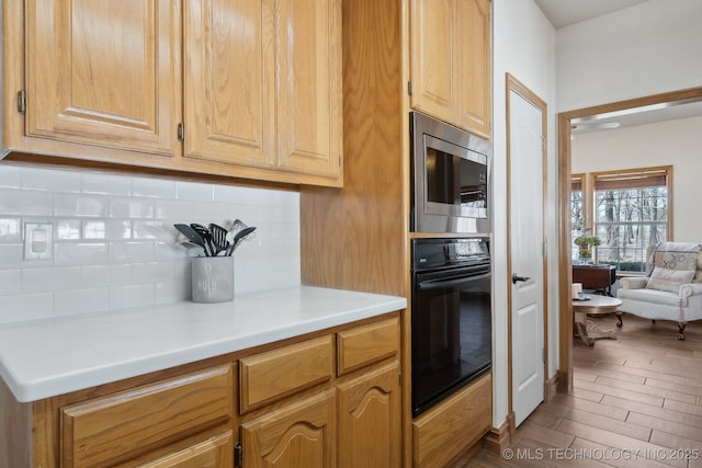 kitchen with stainless steel microwave, light brown cabinetry, double oven, and tasteful backsplash