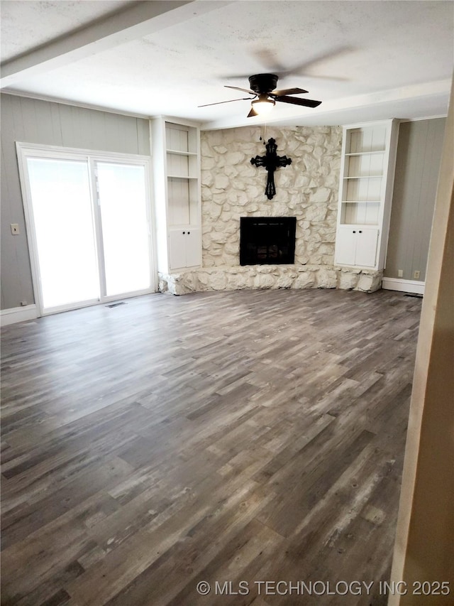 unfurnished living room featuring a stone fireplace, dark hardwood / wood-style floors, wooden walls, built in features, and ceiling fan