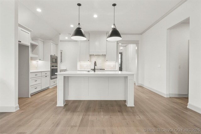 kitchen featuring white cabinets, appliances with stainless steel finishes, decorative light fixtures, light hardwood / wood-style floors, and a kitchen island with sink