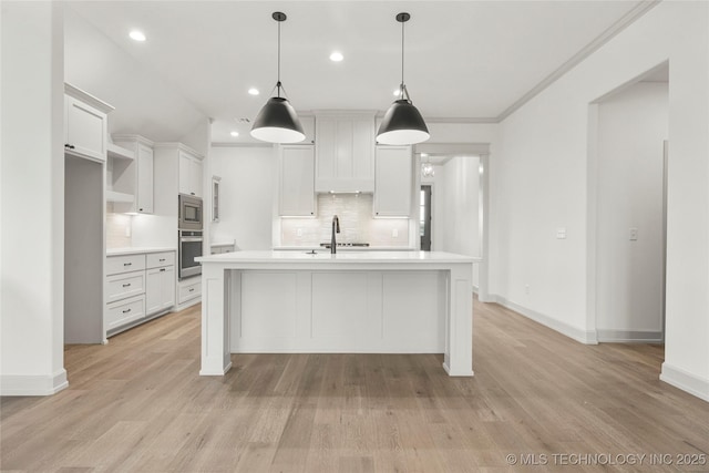 kitchen with appliances with stainless steel finishes, decorative light fixtures, tasteful backsplash, white cabinetry, and a center island with sink