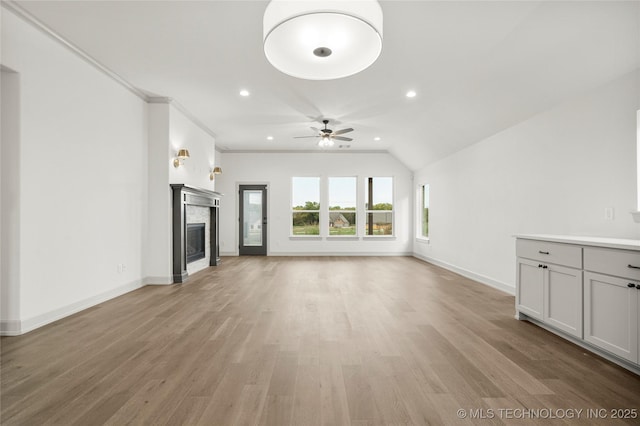 unfurnished living room featuring crown molding, light wood-type flooring, vaulted ceiling, and ceiling fan