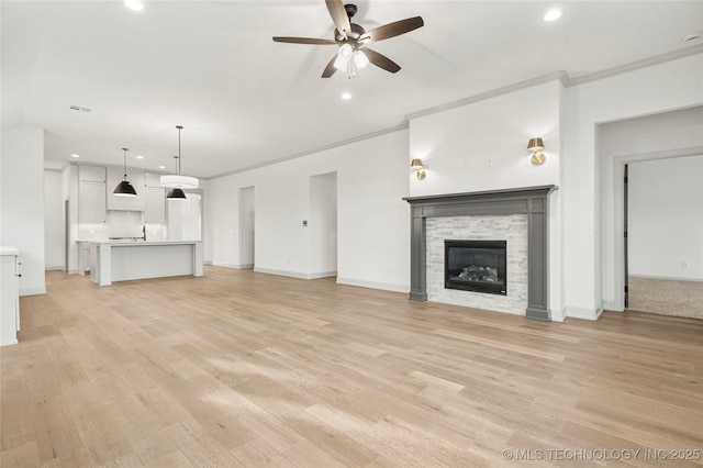 unfurnished living room with ceiling fan, ornamental molding, a stone fireplace, and light hardwood / wood-style floors