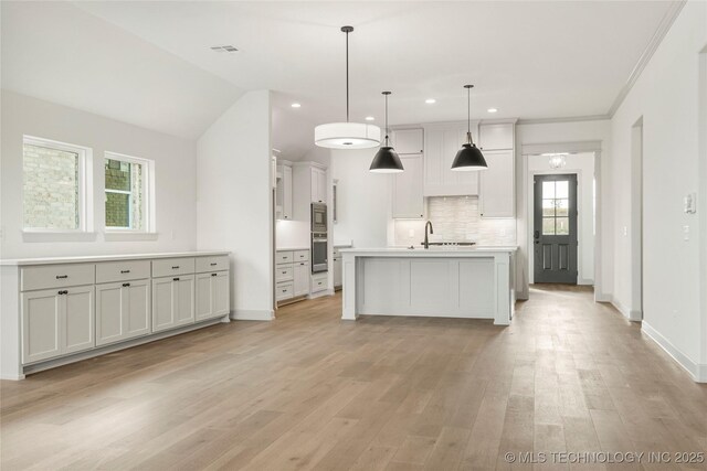 kitchen with hanging light fixtures, light hardwood / wood-style flooring, backsplash, a center island with sink, and lofted ceiling