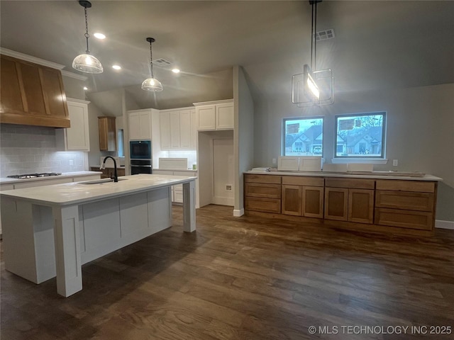 kitchen featuring stainless steel gas stovetop, sink, white cabinets, hanging light fixtures, and a kitchen island with sink