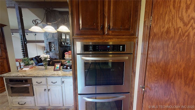 kitchen featuring white cabinetry, stainless steel double oven, light stone counters, and decorative light fixtures