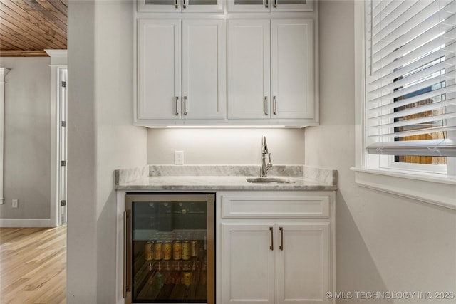 bar with light stone countertops, white cabinets, and beverage cooler