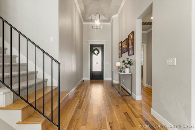 foyer entrance featuring hardwood / wood-style flooring, a high ceiling, a notable chandelier, and ornamental molding