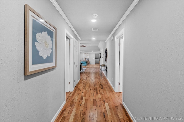 corridor with light hardwood / wood-style flooring and ornamental molding