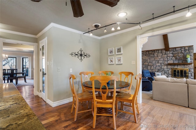 dining space featuring crown molding, a fireplace, a textured ceiling, wood-type flooring, and track lighting