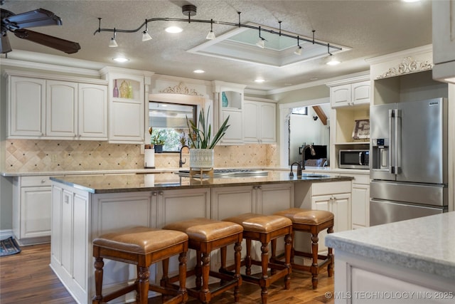 kitchen featuring a kitchen breakfast bar, appliances with stainless steel finishes, white cabinetry, a kitchen island with sink, and ornamental molding