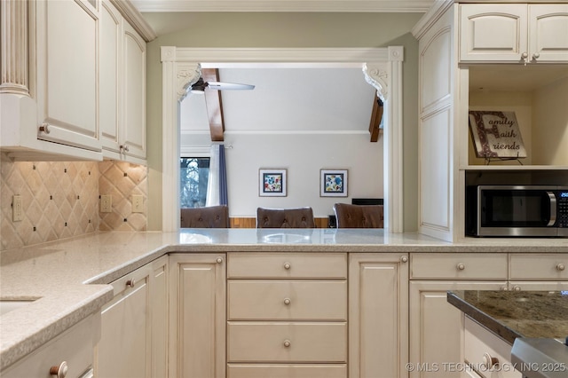 kitchen with cream cabinetry, decorative backsplash, light stone countertops, and ceiling fan