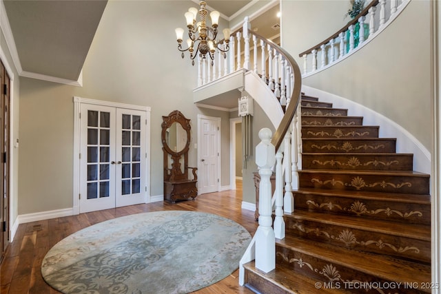 staircase with french doors, a high ceiling, crown molding, and wood-type flooring