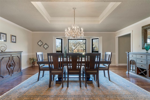 dining area featuring a notable chandelier, ornamental molding, dark wood-type flooring, and a tray ceiling