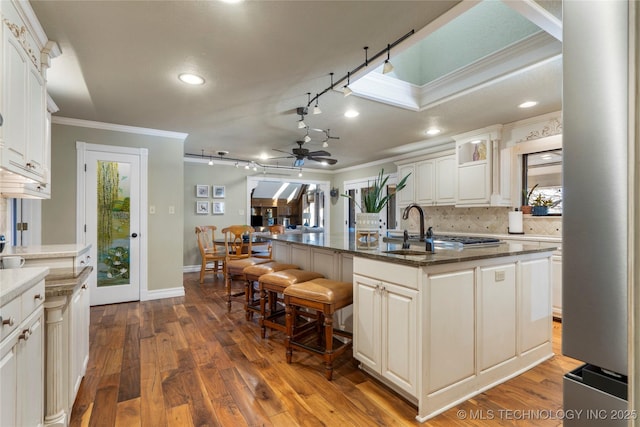 kitchen with crown molding, a kitchen island with sink, white cabinets, dark stone countertops, and sink