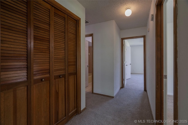 hallway with light colored carpet and a textured ceiling