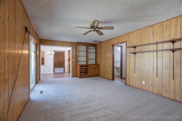 carpeted spare room with ceiling fan with notable chandelier, a textured ceiling, and wood walls