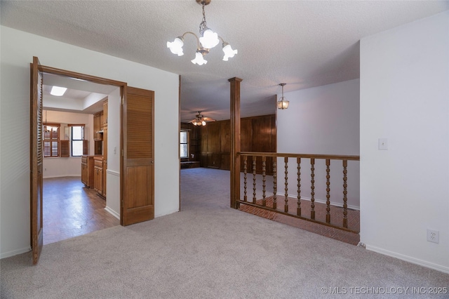 empty room with ornate columns, ceiling fan with notable chandelier, light colored carpet, and a textured ceiling