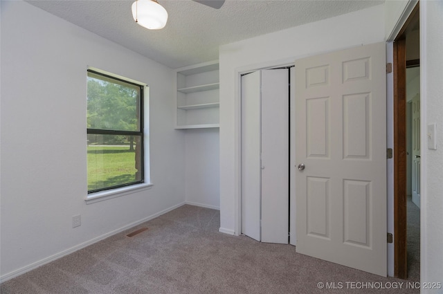 unfurnished bedroom featuring light carpet, multiple windows, a textured ceiling, and a closet