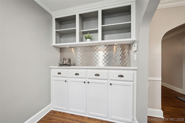 bar with decorative backsplash, dark wood-type flooring, white cabinets, and ornamental molding