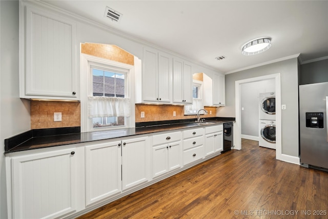 kitchen with stainless steel refrigerator with ice dispenser, white cabinetry, sink, plenty of natural light, and stacked washing maching and dryer