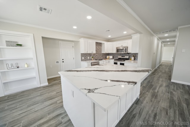 kitchen featuring stainless steel appliances, light stone counters, ornamental molding, white cabinets, and a kitchen island