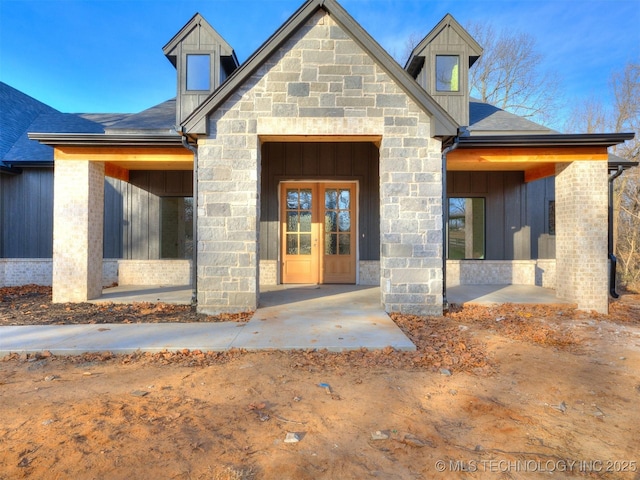 view of exterior entry featuring french doors, stone siding, board and batten siding, and a shingled roof