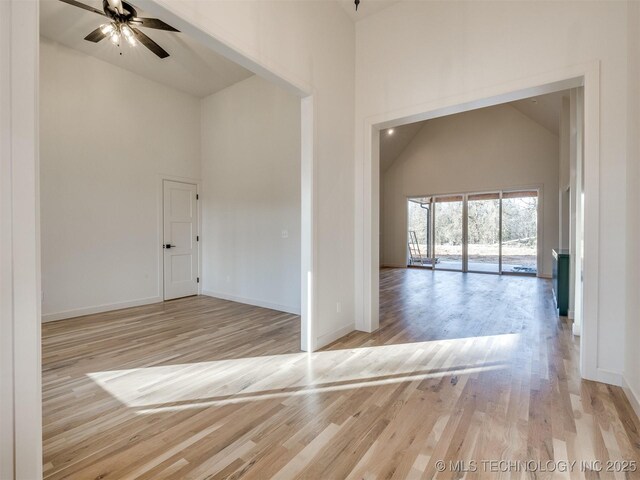 spare room with light wood-style floors, baseboards, high vaulted ceiling, and a ceiling fan