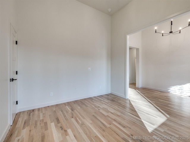 unfurnished room featuring baseboards, light wood finished floors, and a chandelier